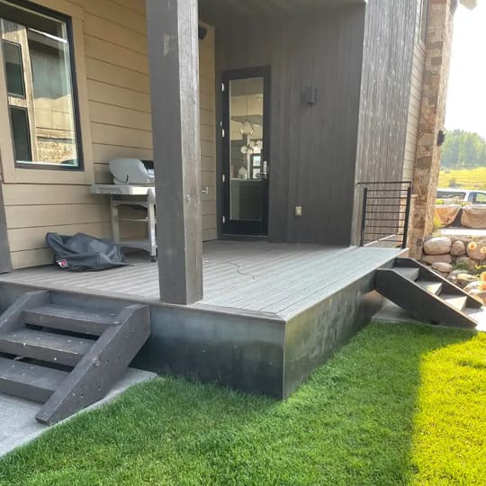 Small covered back porch with composite steps on a tan house with dark board-and-batten siding