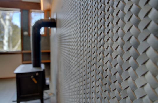 Close-up of a basket-weave tile wall with a black wood stove in soft focus behind it