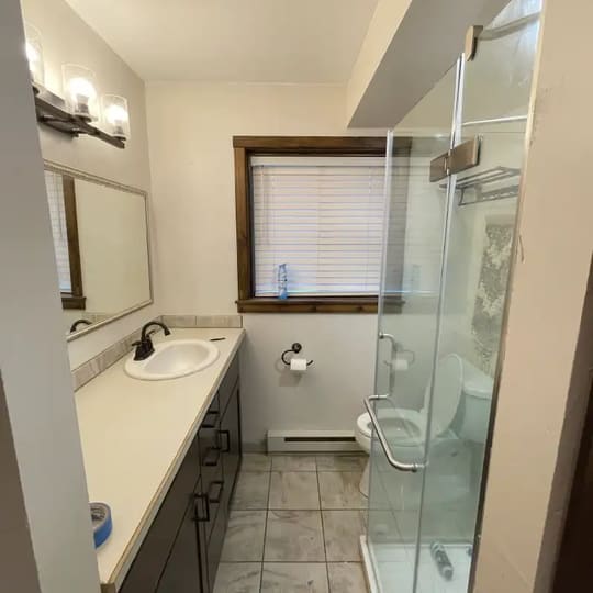 Bathroom with a frameless glass shower door, white walls and a gray marble-look tile floor