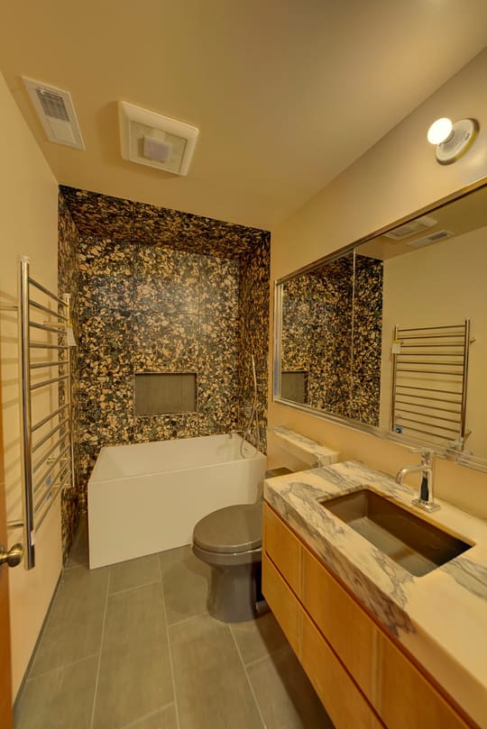 Bathroom with a speckled tile tub surround, a white soaking tub, a floating vanity and a chrome towel warmer