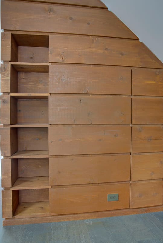 Wall of custom wood drawers and open cubbies fitted under a sloped ceiling