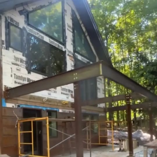 Metal beams framing a new deck against a house wrapped for siding