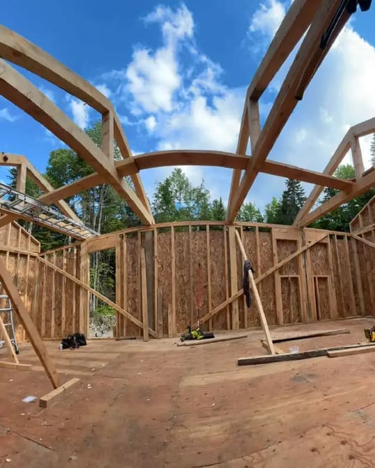 Curved timber roof trusses being framed on a house under a blue sky