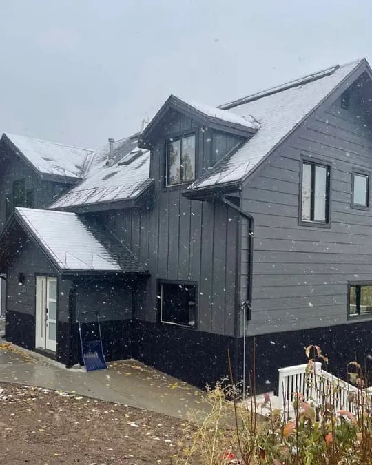 Two-story home with gray siding and black trim in a snowy yard