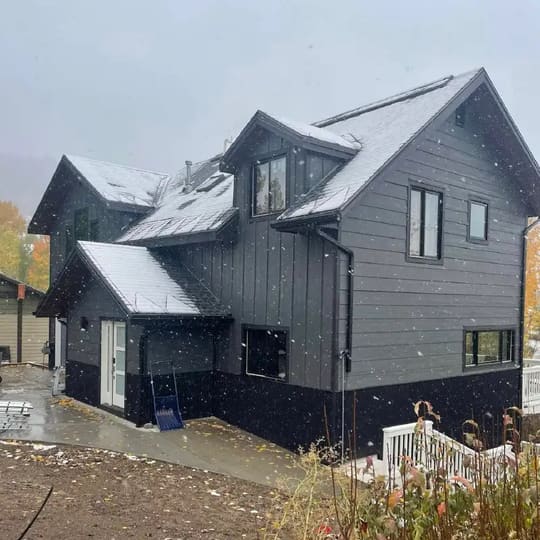Two-story home with gray siding and black trim in a snowy yard