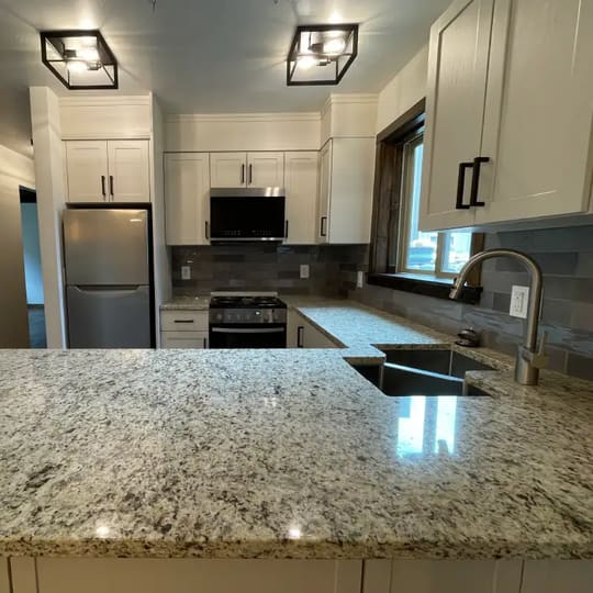 Kitchen with white cabinets, granite countertops and a corner sink under a window