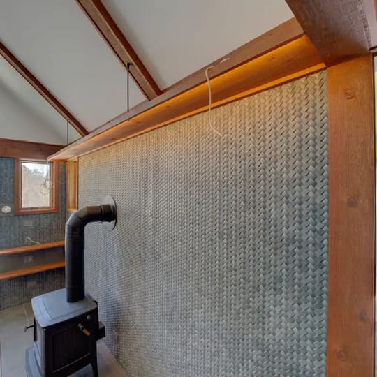 Living room with a woven gray tile wall, a black wood stove and orange-stained ceiling beams