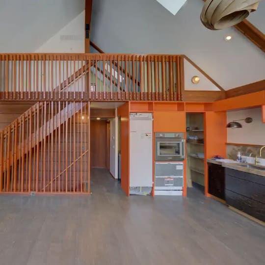 Kitchen with a wood-slat loft railing above and orange-stained trim