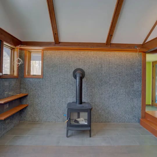 Black wood stove against the woven tile wall under orange-stained beams