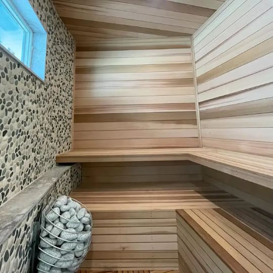 Sauna interior with tiered wood benches and a stacked-stone heater wall