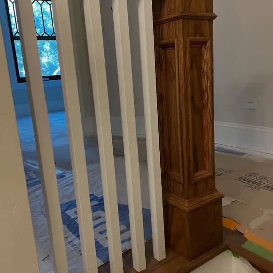 Dark-stained wood newel post with white spindles on a staircase