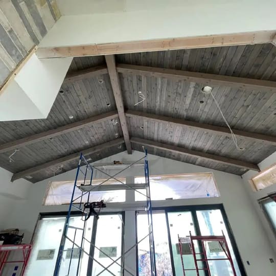 Vaulted ceiling clad in gray wood paneling above tall windows, with scaffolding in place