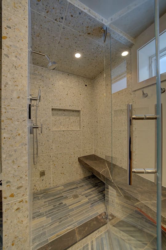 Glass shower door opening onto a tiled walk-in shower with a floating bench